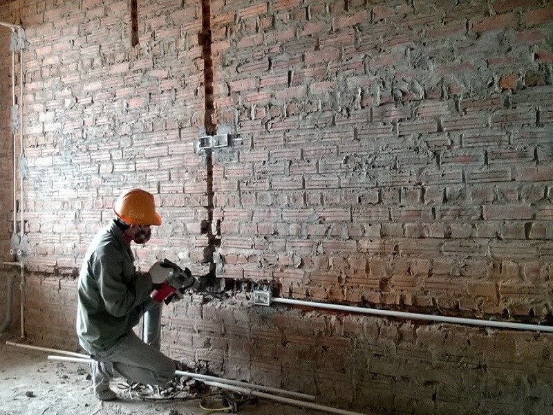 Công nhân đội mũ bảo hộ đang dùng máy đục tường gạch đỏ trơ trọi trong công trình xây dựng.