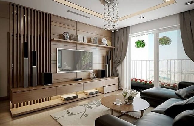 Phòng khách hiện đại với nội thất gỗ, sofa da, bàn tròn nhỏ và cửa kính lớn nhìn ra ban công với cây xanh.